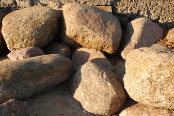 Stones on the shore against the wall.
Large stones lie close to each other against the wall on the shore of the Gulf of Finland. The setting sun illuminates the stones. The stones cast shadows on each