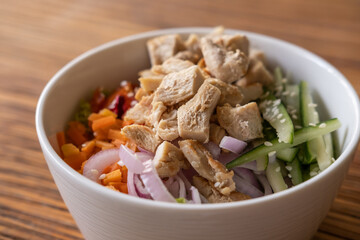 Healthy organic chicken poke bowl with cucumber, rice, carrots, onion served in bowl on wooden table. Healthy lifestyle