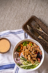 Healthy organic vegetarian poke bowl with tofu, fermented soybeans- tempeh, cucumber, rice, carrots, onion served in bowl on table decorated with kitchen napkin. Healthy lifestyle