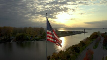 Patriotic scene of American flag waving while being backlit by sunset, Cinematic Aerial American Flag sunset clip - Powered by Adobe