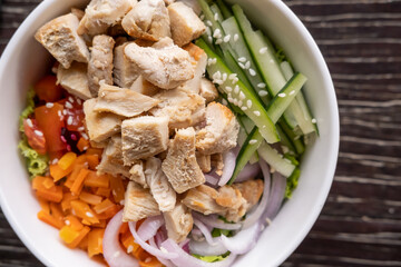 Healthy organic chicken poke bowl with cucumber, rice, carrots, onion served in bowl on wooden table. Healthy lifestyle