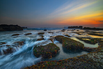 Amazing seascape. Ocean with moving wave. Low tide. Stones covered by green moss and seaweeds. Concept of nature background. Sunset scenery. Long exposure. Mengening beach, Bali