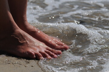 female feet on the beach in the waves of sea water with foam
