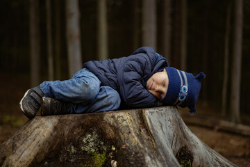 A close up portrait of cute little caucasian boy pretending sleeping, cuddling on big stub in a forest.