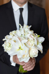 The groom holding a wedding bouquet of flowers in his hands, waiting for his bride. bridal bouquet of white lilies and daisies