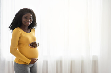 Beautiful pregnant african woman hugging her big belly at home
