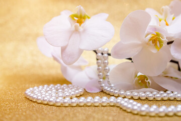 Fototapeta na wymiar White Orchid and pearl necklace on a shiny gold background 