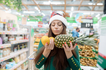 Young woman in a santa hat holds fragrant tangerines and pineapple in her hands
