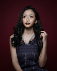 Fototapeta premium Beauty Asian Woman with Perfect Makeup. Beautiful Girl face isolated on dark red background. Glamor fashion model with bright gloss make-up poses in the studio. Stylish fashionable concept.
