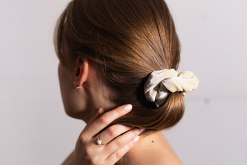 Natural blond woman holding her amazing hair in ponytail with beige scrunchie. Side perspective. White background.