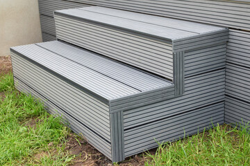Part of dark gray or anthracite wpc composite material terrace deck with stairs  in backyard green grass outdoors.
