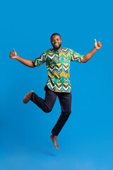 Fototapeta premium Positive black man jumping up over blue