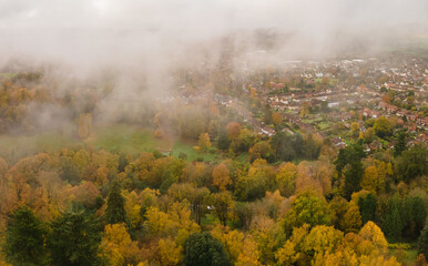 Aerial view of the edge of an English town and beautiful autumn trees with low hanging morning mist