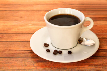 On a hard surface is a white cup and saucer of hot aromatic black Americano coffee.