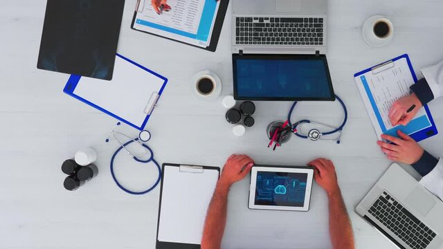 Top view of medical specialist checking appointment on flatfly using digital technology in clinic. Team doctors on desk table with stethoscope and devices working in hospital on copy space.