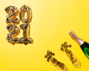 2021 gold balloons and Champagne bottle and flute glasses with gold stars confetti on yellow paper...