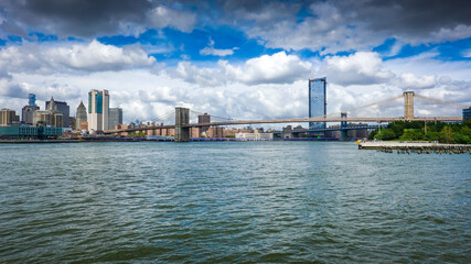 View from Brooklyn Bridge to Manhattan in New York during sunny day with blue sky and white clouds