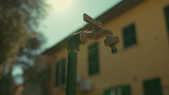cinematic dolly shoot of an outdoor tap slow water dripping. Leaking tap water. Help save water. shot in slow motion