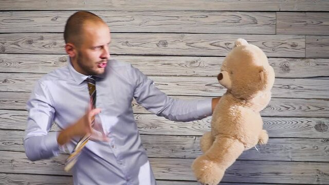 Young angry businessman beating a stuffed bear toy in his office. Concert on the theme of frustration