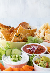 Various popular appetizer dips with crisp bread and vegetables for dipping.