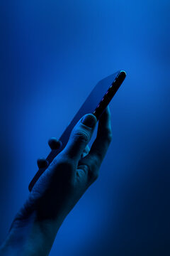 Hand holds smartphone. Neon classic blue light, vertical photo.