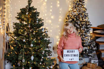 Attractive blonde woman holding a panel with Merry Christmas congratulation.