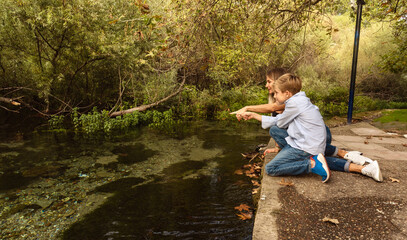 Woman and her son sitting at park by the pond and pointing far away.