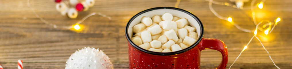 Banner of Red cup of hot cocoa with marshmallows and candy canes. background with beautiful Christmas lights bokeh.