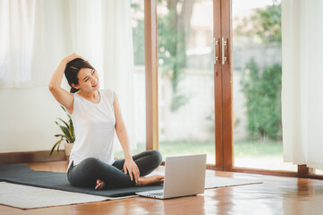 Smiling Asian woman doing yoga neck stretching online class from laptop at home in living room....
