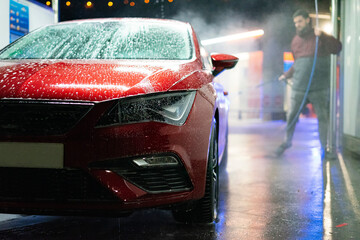 Man washing a red car with high pressure water in a car wash.