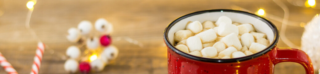 Banner of Red cup of hot cocoa with marshmallows and candy canes. background with beautiful Christmas lights bokeh.