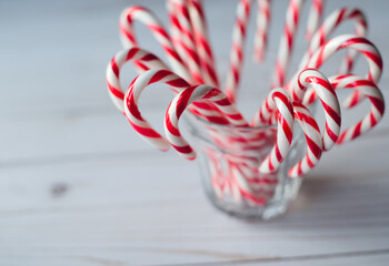 Close up of a cup full of candy canes on white weathered wood table.