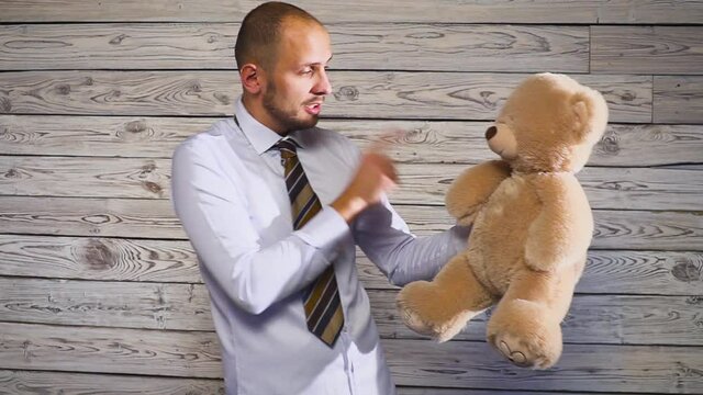 Young angry businessman beating a stuffed bear toy in his office. Concert on the theme of frustration