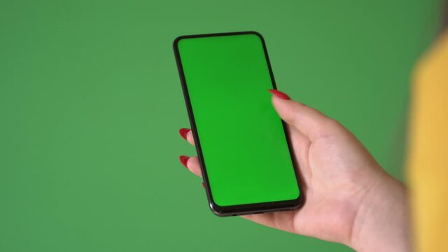 Woman hand holding the smartphone on green screen chroma key background. Mobile phone mock-up for your product. The iPhone Xr model in vertical orientation portrait mode