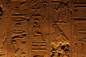 Ancient egyptian stone carvings on the walls of Luxor Temple in Egypt, with pictures of owl, eye, pharaoh figures and hieroglyphs symbols