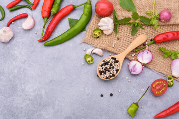 Pepper in a wooden spoon and red chilies shallots garlic basil coriander leaves and tomatoes placed on the table top - top view.