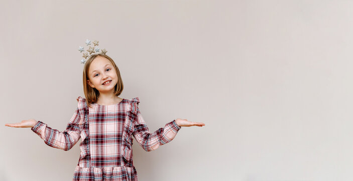 10-year-old girl on a beige background smiling, hands to the sides.