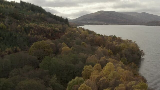 An aerial view looking down Loch Tay on an autumn day, Stirling, Scotland. Flying sleft to right over shorline trees to reveal the town of Killin in the distance.