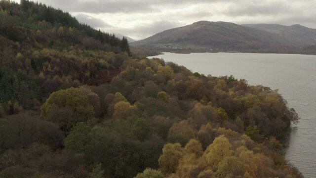 An aerial view looking down Loch Tay on an autumn day, Stirling, Scotland. Flying sleft to right over shorline trees to reveal the town of Killin in the distance whilst slowly zooming in.