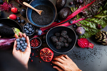 Purple raw vegetables and fruits on black background and a hand holding blueberries