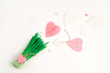Decorative bouquet of green grass and hearts on a light background. Top view with space to copy. Concept of holiday backgrounds.