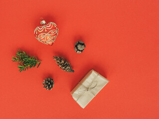 Christmas flat lay on red background. Eco gift wrapped in recycled paper, trees cones, heart shaped Christmas ball.