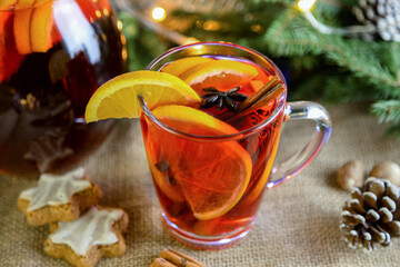 A glass of hot mulled wine with fresh orange slices and cinnamon sticks nearby on a beige background. New Year's, winter drink