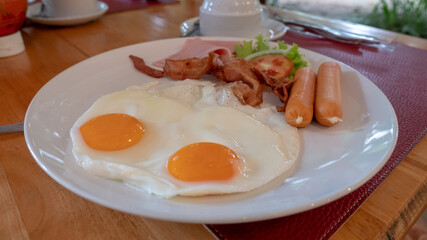 closeup fried egg, sausage and ham on white plate