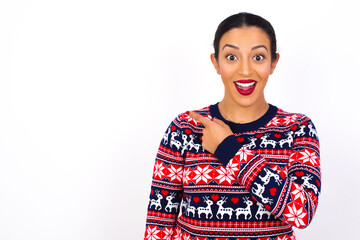 Young beautiful Arab woman wearing Christmas sweater against white wall pointing away and smiling to you. Look over there!