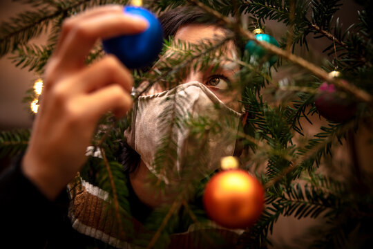 Woman is decoration a christmas tree with baubles while she wearing a face mask, corona