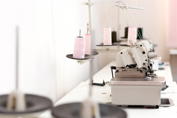 Detailed image, close up of professional sewing equipment and sewing thread. Industrial textile machines in a row. Sewing machine with overlock. Equipment for tailors shop, sewing factory. Industrial