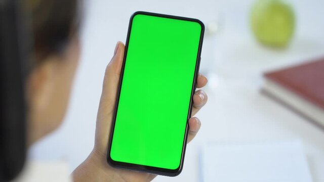 Close-up shot of green screen template smartphone in female hands at home offise, girl is watcing content, makes notes in a notebook. Modent technology and information concept.