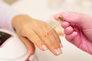 Close-up of a manicurist applying moisturizing nail oil on person's hand.