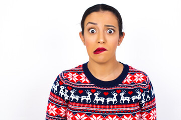 Young beautiful Arab woman wearing Christmas sweater against white wall being nervous and scared biting lips looking camera with impatient expression, pensive.